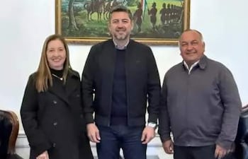 Carmen Giménez de Ovando, Pedro Alliana y Agustín Ovando interactúan en oficina elegantemente decorada con banderas de Paraguay.