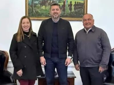 Carmen Giménez de Ovando, Pedro Alliana y Agustín Ovando interactúan en oficina elegantemente decorada con banderas de Paraguay.