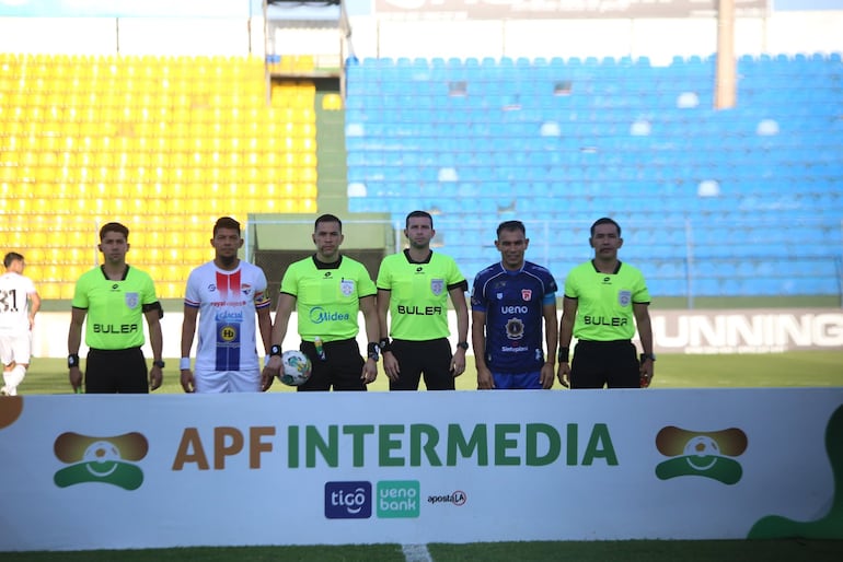 Los capitanes de ambos equipos posan con la terna arbitral en cancha.