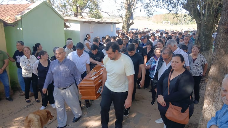 Hombres y mujeres de luto acompañan un féretro de madera, en un camino de tierra, expresando tristeza y respeto en la ceremonia.