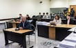 Hugo Ramírez, con abrigo oscuro y barba, habla al micrófono en una sala de tribunal; una mujer toma notas a su lado.