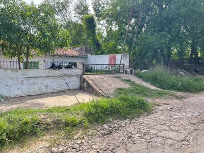 Ambiente tranquilo en Itay con cercas metálicas, casa blanca y vegetación exuberante, sin personas presentes.