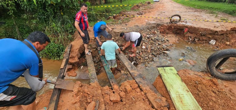 Cinco hombres trabajando en reparación de camino, uno con camiseta azul, otro con rayas rojas, otros con camisetas verdes y grises.