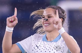 Jugadora del Club Libertad con camiseta blanca y azul, levantando el dedo índice en gesto de celebración en fondo deportivo azul.