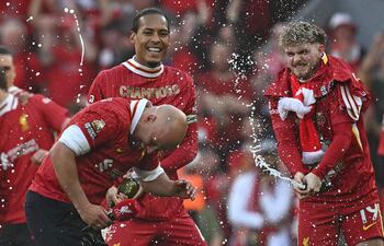 Liverpool's Dutch manager Arne Slot reacts as Liverpool's Dutch defender #04 Virgil van Dijk (L) and Liverpool's English midfielder #19 Harvey Elliott spray him with champagne after the English Premier League football match between Liverpool and Tottenham Hotspur at Anfield in Liverpool, north west England on April 27, 2025. Liverpool won the match 5-1, making them the winners of the Premier League title. (Photo by Paul ELLIS / AFP) / RESTRICTED TO EDITORIAL USE. No use with unauthorized audio, video, data, fixture lists, club/league logos or 'live' services. Online in-match use limited to 120 images. An additional 40 images may be used in extra time. No video emulation. Social media in-match use limited to 120 images. An additional 40 images may be used in extra time. No use in betting publications, games or single club/league/player publications. /