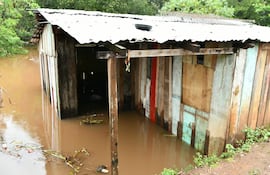 Vivienda de madera parcialmente sumergida en agua marrón, rodeada de vegetación densa en un entorno rural.
