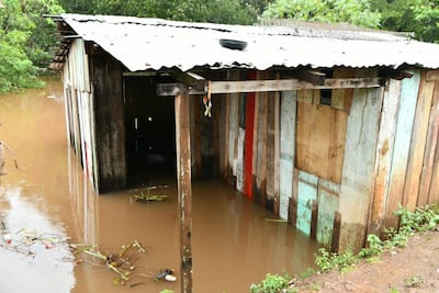 Vivienda de madera parcialmente sumergida en agua marrón, rodeada de vegetación densa en un entorno rural.