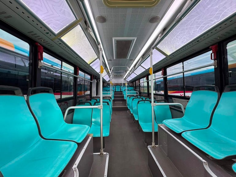 Interior de un autobús moderno y desocupado con asientos turquesas y amplias ventanas luminosas.