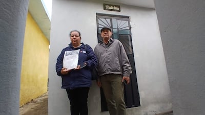 Felicia Ramona Benítez Aguilera con chaqueta azul, sosteniendo un documento, mientras un hombre con sombrero gris se encuentra a su lado.