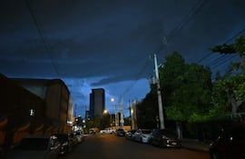Calle urbana iluminada por faroles bajo una tormenta; vehículos estacionados y árboles a un lado.