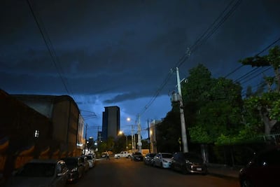 Calle urbana iluminada por faroles bajo una tormenta; vehículos estacionados y árboles a un lado.