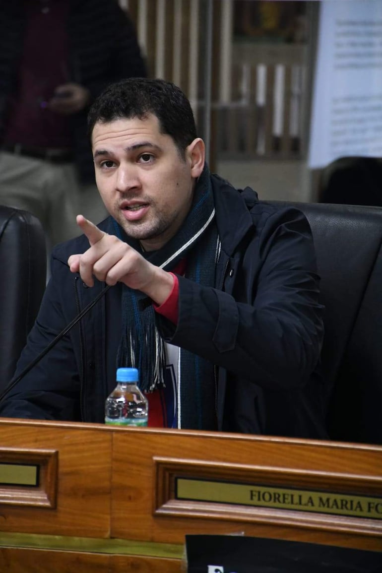 Pablo Callizo con camiseta blanca y bufanda, señalando mientras critica el uso de bienes municipales en una reunión formal.