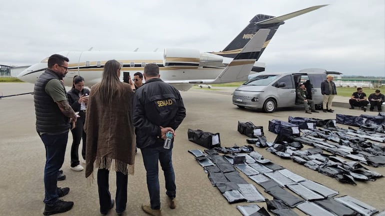 El director de Seguridad del aeropuerto Silvio Pettirossi, Gustavo Sandoval (con chaleco); la fiscala de Narcotráfico de Asunción, Ingrid Cubilla (con un poncho), y un agente especial de la Senad (campera de la institución) en el lugar de la incautación de marihuana premium.