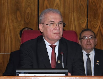 Emiliano Rolón Fernández en chaqueta oscura y corbata roja habla frente a un micrófono; otro hombre observa atentamente.