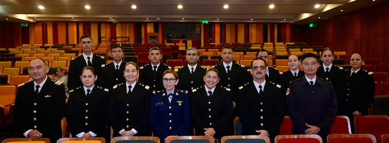 Catorce personas en uniforme oscuro con insignias doradas organizadas en filas. Una mujer en uniforme azul destaca en el centro.