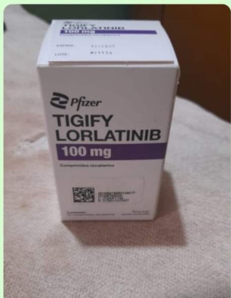 Caja de medicamento Tigify Lorlatinib sobre superficie textil, con fondo difuso.