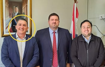Hans Kemper con traje azul, Patrick Kemper en abrigo oscuro y Hugui Farías en traje oscuro, todos sonriendo en un despacho con bandera paraguaya.