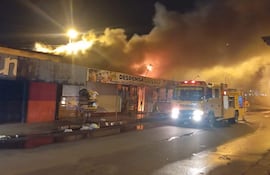 Escena de un incendio en la lomitería 'Despenza Deisy', con humo y llamas visibles. Vehículo de bomberos en la calle.