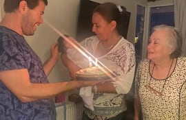 Mujer sonriente sostiene un pastel de cumpleaños mientras un hombre acaricia la cabeza de un bebé en brazos. Ambiente festivo.