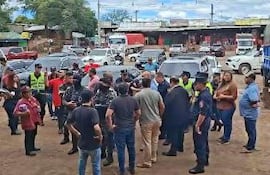 Grupo de veinte personas, algunas con ropa de seguridad, conversan en un área comercial al aire libre, con ambiente urbano y árboles de fondo.
