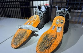 Zapatos negros sobre superficie plana con frascos pequeños dentro y cinta adherida a uno de ellos, en un entorno cerrado.