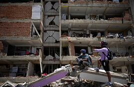 Varias personas permanecen de pie sobre los escombros frente a un edificio de varios pisos dañado en Catia La Mar, La Guaira, Venezuela.
