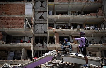 Varias personas permanecen de pie sobre los escombros frente a un edificio de varios pisos dañado en Catia La Mar, La Guaira, Venezuela.