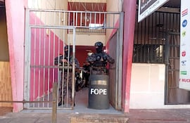 Dos agentes de la FOPE en equipamiento táctico y armas largas, en la entrada de un edificio con paredes rosas y un cartel visible.