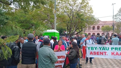 Mujer sonriente en camiseta rosa y hombre con capa roja sostienen carteles en manifestación al aire libre.