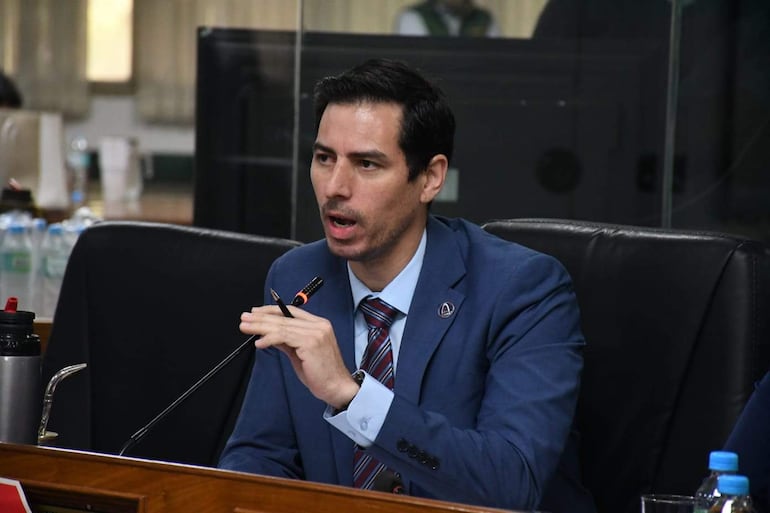 Alvaro Grau en traje azul gesticulando con una mano, mientras sostiene un bolígrafo, en un ambiente de reunión formal.