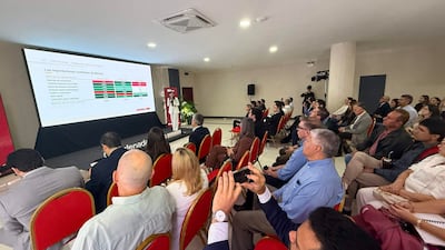 Mujer en traje blanco presenta datos en proyector, con asistentes tomando notas en un ambiente profesional.
