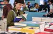 Una joven escoge un libro en una feria del libro.