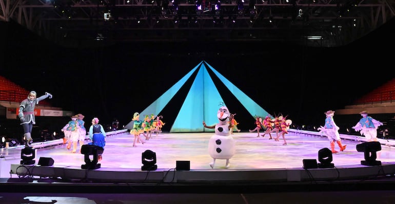 Bailarines vestidos de coloridos trajes sobre hielo, iluminados por luces brillantes en un ambiente festivo.