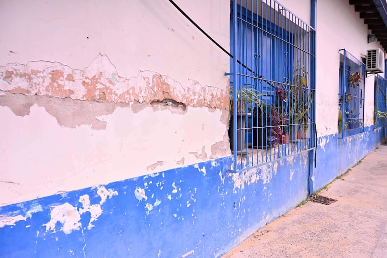 Pared exterior de la Escuela República Oriental del Uruguay con pintura descascarada y rejas azules, sin personas visibles.