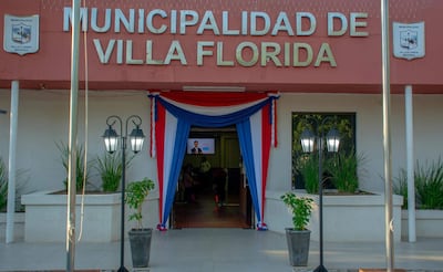 Fachada de la Municipalidad de Villa Florida decorada con drapeados en azul, rojo y blanco, con plantas y lámparas a los lados.
