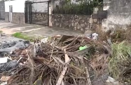 Montículo de basura desordenado cerca de una acera pavimentada y una pared de piedra, sin personas presentes.