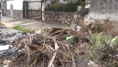 Montículo de basura desordenado cerca de una acera pavimentada y una pared de piedra, sin personas presentes.