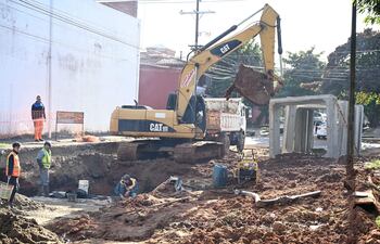 Trabajadores con chalecos de seguridad en obra de construcción, manipulando herramientas y operando excavadora CAT amarilla.