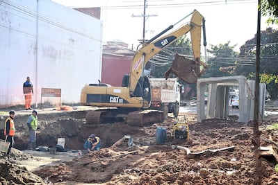 Trabajadores con chalecos de seguridad en obra de construcción, manipulando herramientas y operando excavadora CAT amarilla.