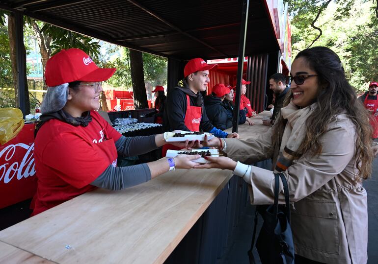 Mujer sonriente con gorra roja recibe comida de voluntario con camiseta roja en un ambiente natural.