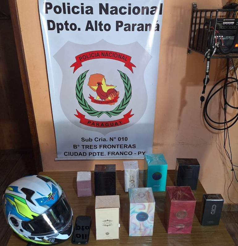 Ambiente policial con casco de motocicleta y cajas de perfumes sobre una mesa. Sin personas visibles.
