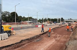 Cinco trabajadores en chalecos reflectantes en obra, manipulando herramientas y supervisando maquinarias en un entorno nublado.