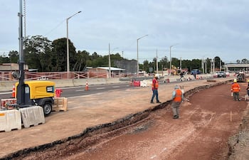 Cinco trabajadores en chalecos reflectantes en obra, manipulando herramientas y supervisando maquinarias en un entorno nublado.