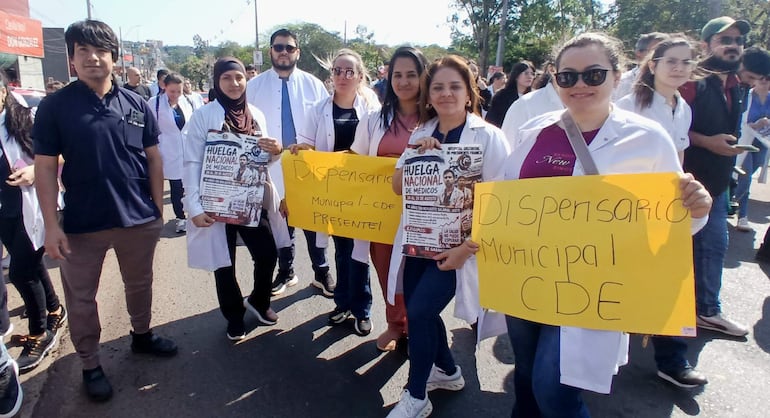 Grupo de médicos con batas blancas sostiene carteles en una calle, visiblemente comprometidos en la manifestación.