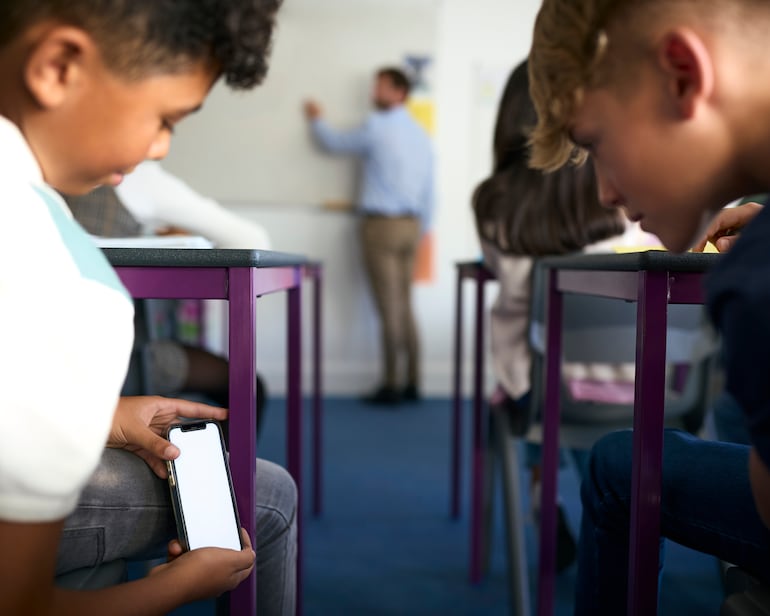 Dos niños revisan un teléfono celular en el aula.
