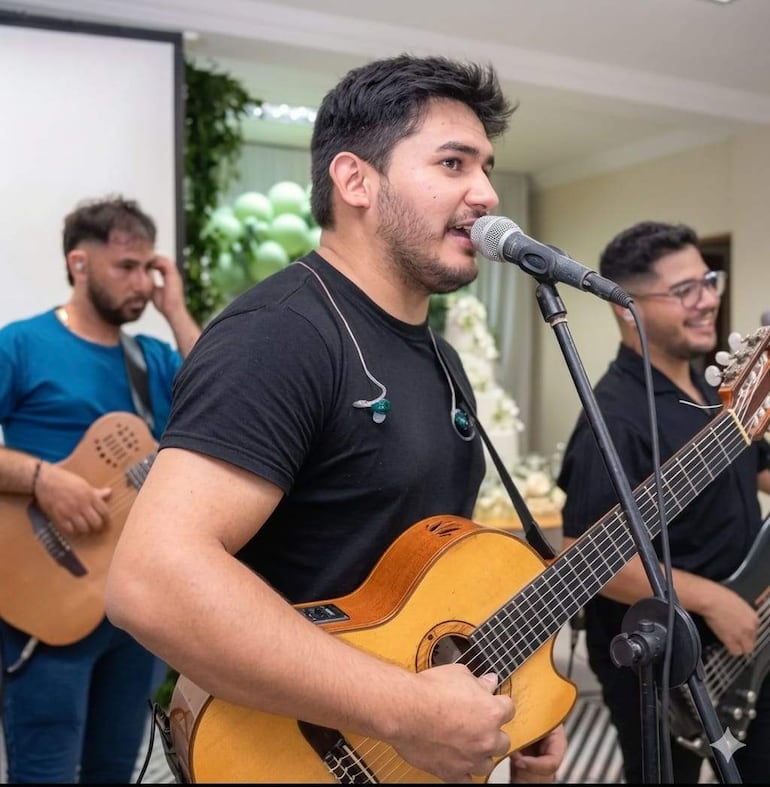 Elías Coronel en camiseta negra canta al micrófono, acompañado de músicos en un ambiente festivo con globos.