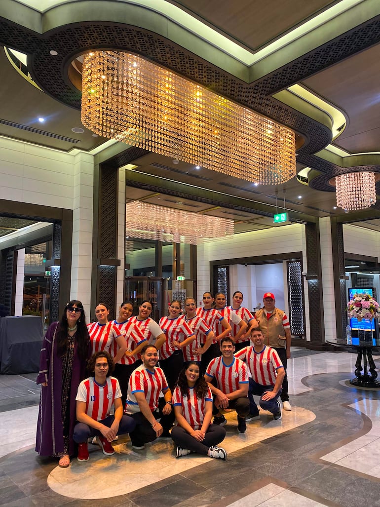 Grupo de 14 personas, hombres y mujeres, posan sonrientes con camisetas rojas y blancas, en un ambiente social elegante.
