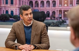 Santiago Peña Palacios sentado con chaqueta marrón y suéter azul, mientras un hombre escucha atentamente en un ambiente de oficina.