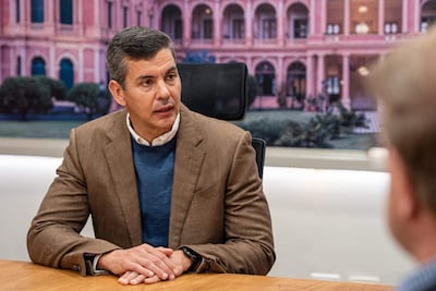 Santiago Peña Palacios sentado con chaqueta marrón y suéter azul, mientras un hombre escucha atentamente en un ambiente de oficina.