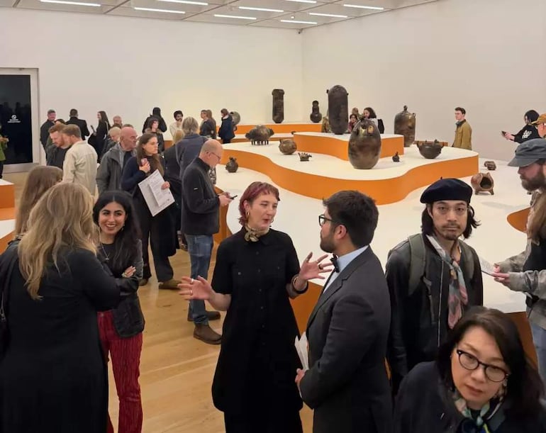 Julia Isídrez, mujer de cabello corto y rojo, gesticula mientras habla con un hombre de chaqueta y corbata, rodeados de público en un museo.